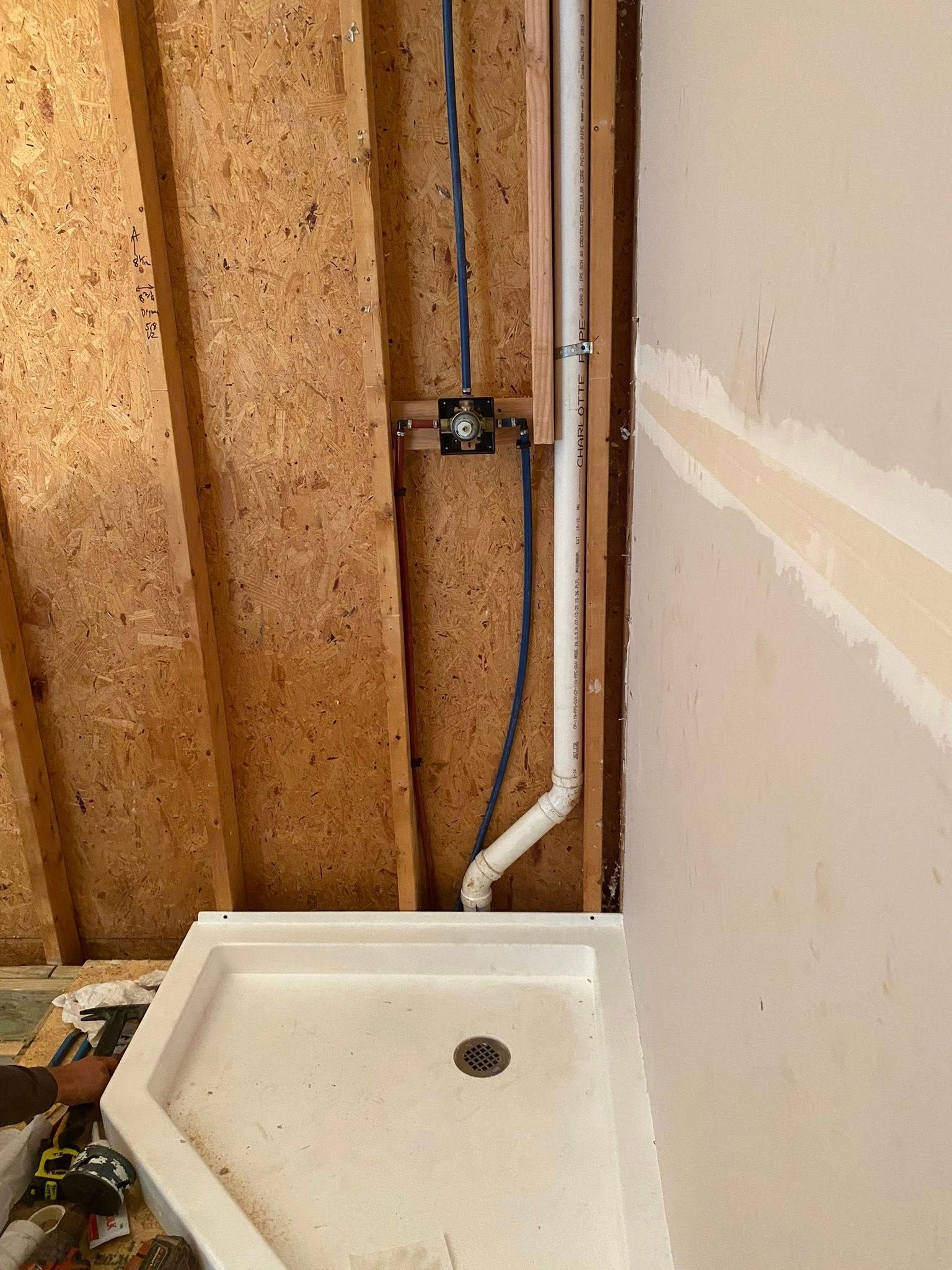 Shower base and plumbing against unfinished walls. Electrical box and drainpipe visible.