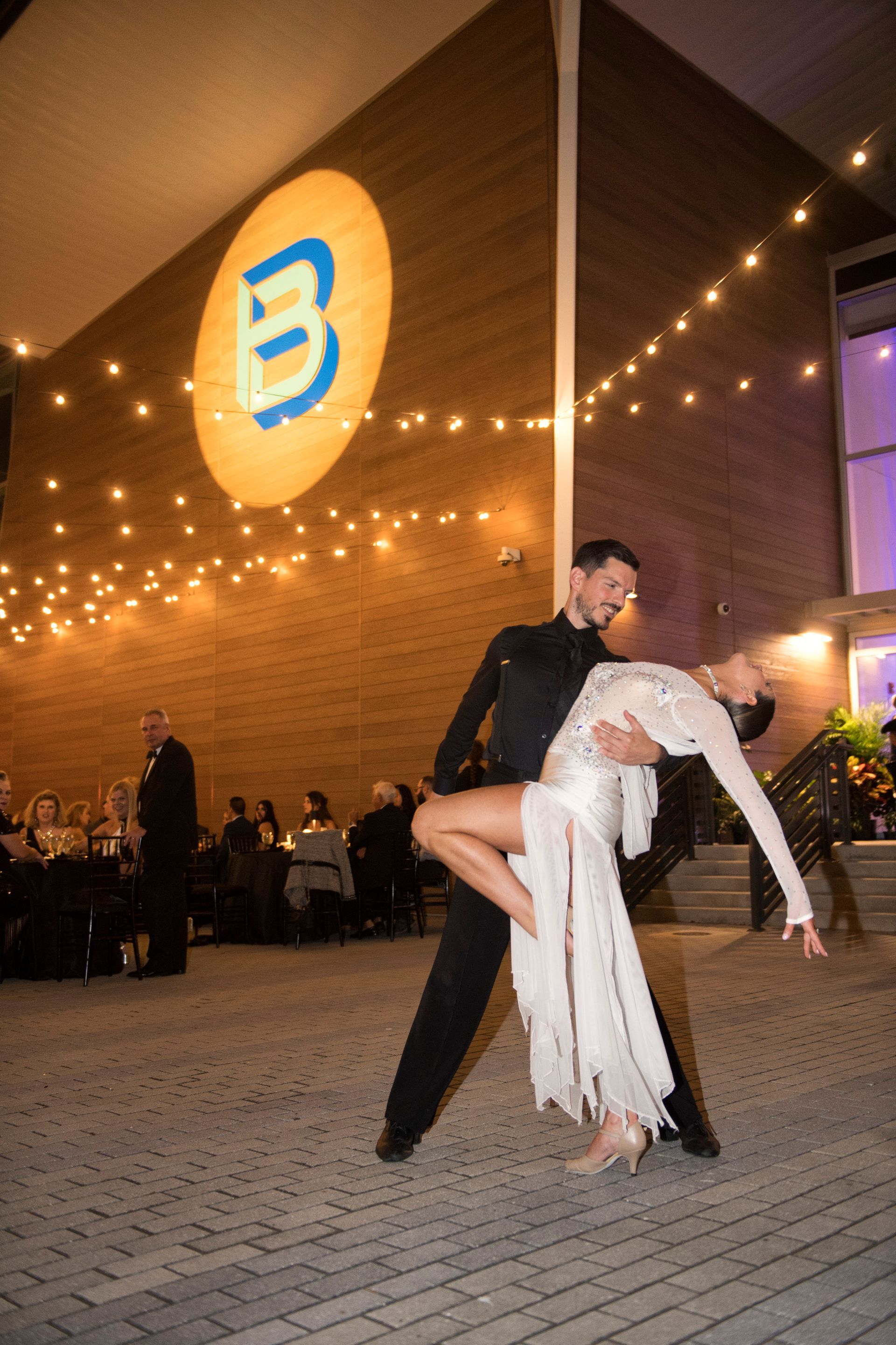 A man is holding a woman in his arms while dancing in front of a building.