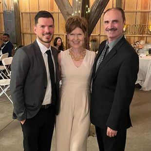 Two men and a woman are posing for a picture at a wedding reception.
