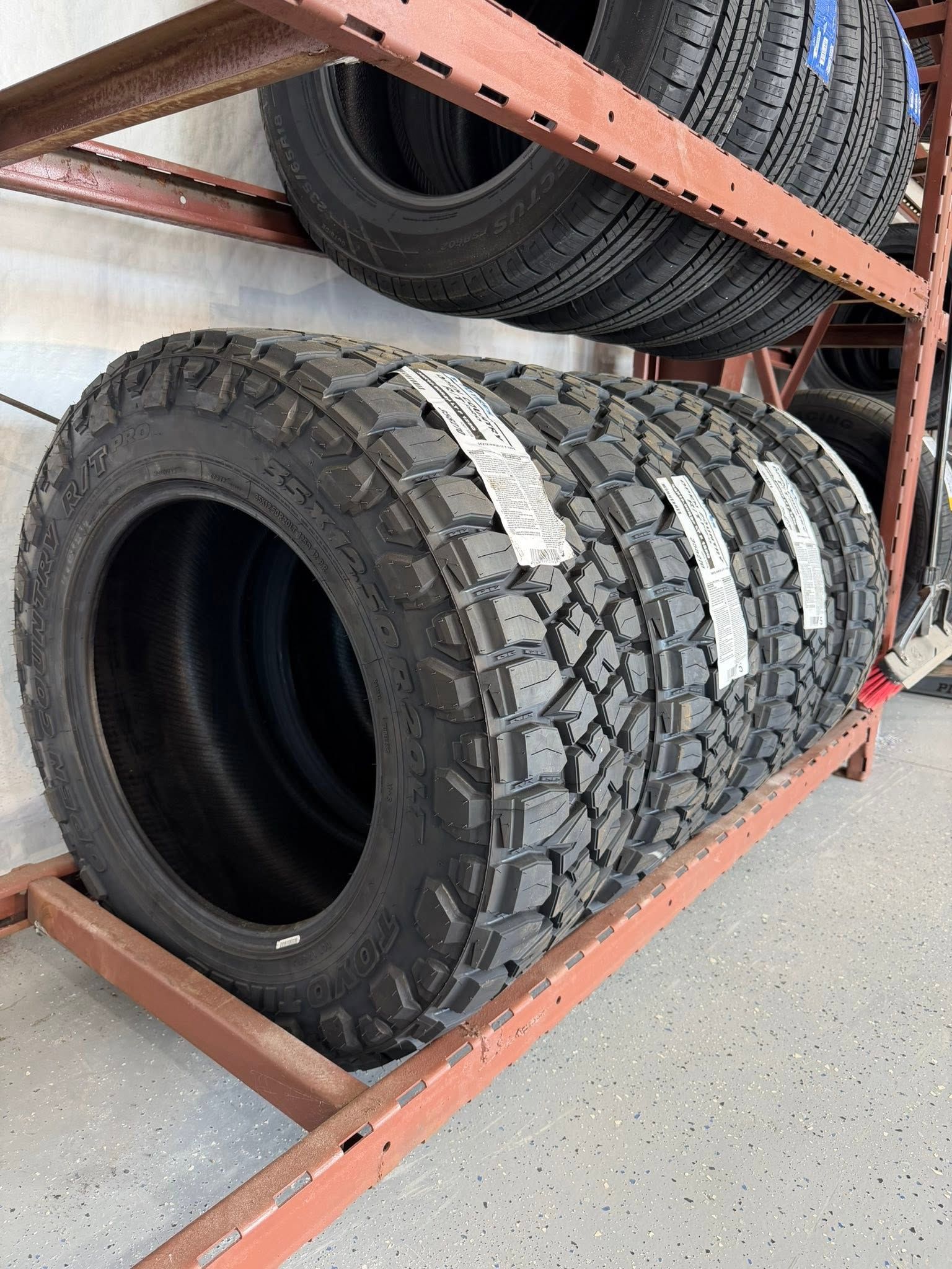 Large off-road tires stacked on a red metal warehouse rack
