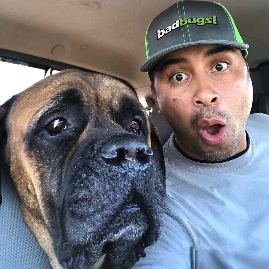 A man wearing a hat that says gotbugs is sitting next to a dog