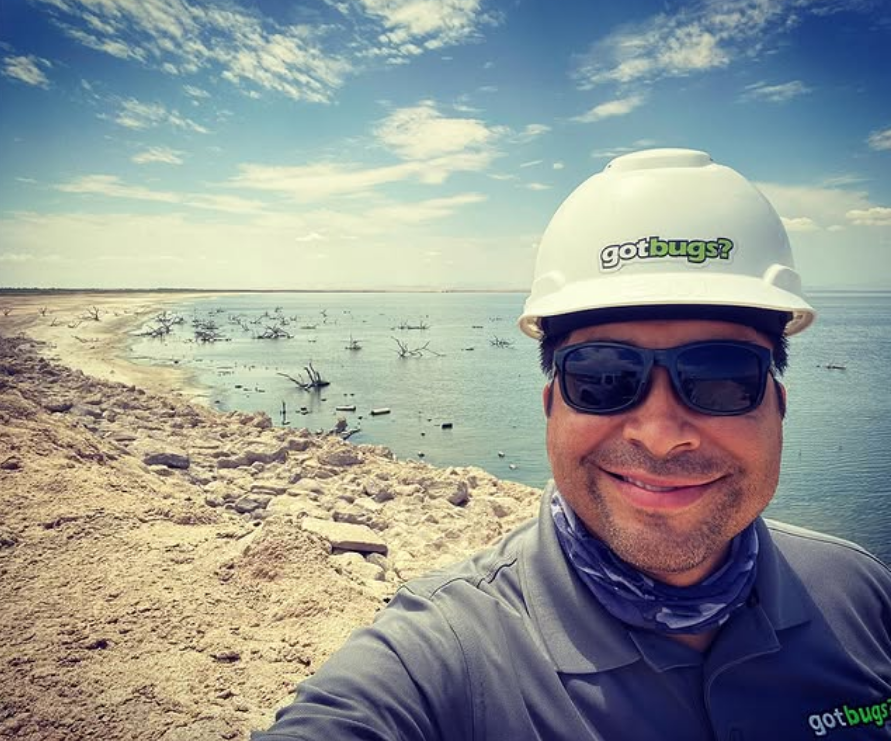 A man wearing a hard hat and sunglasses is taking a selfie
