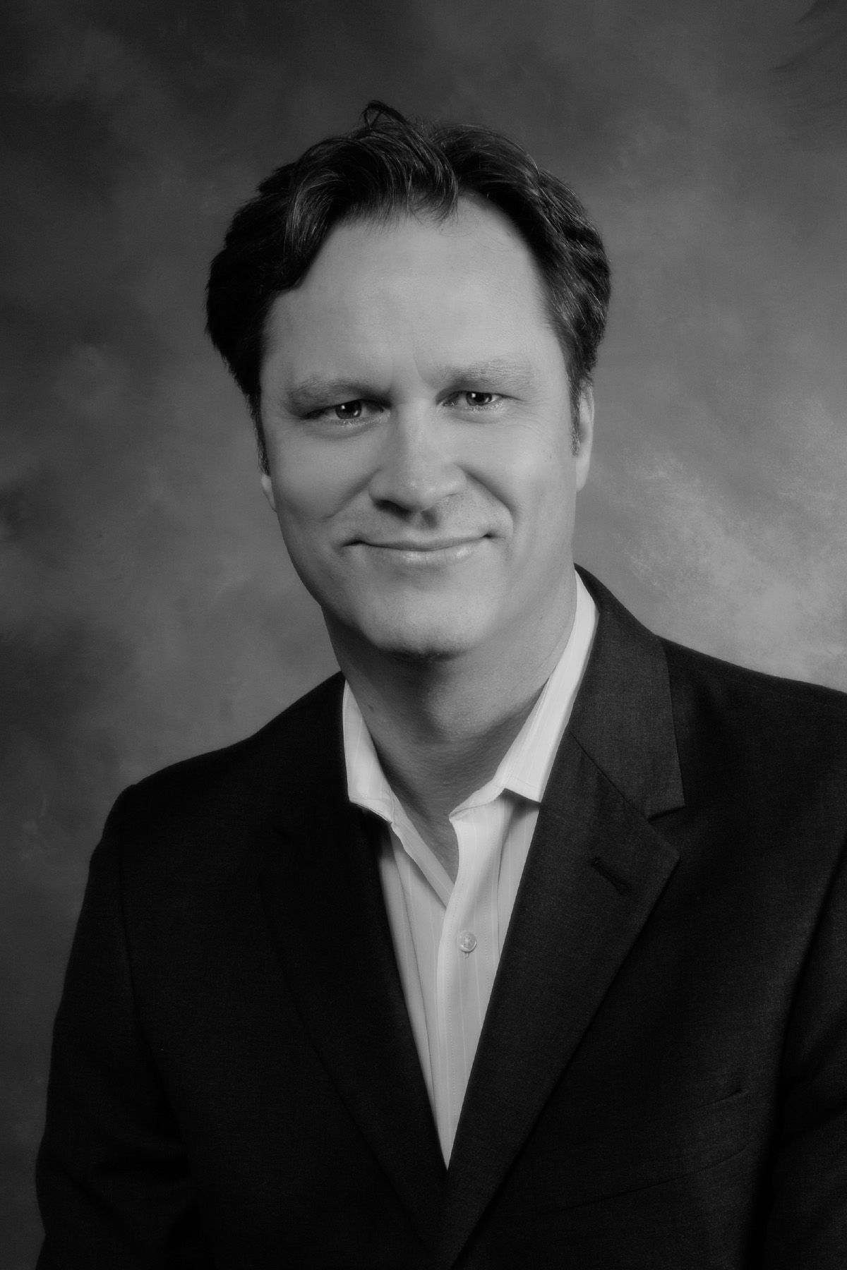 A man in a suit and white shirt is smiling in a black and white photo.