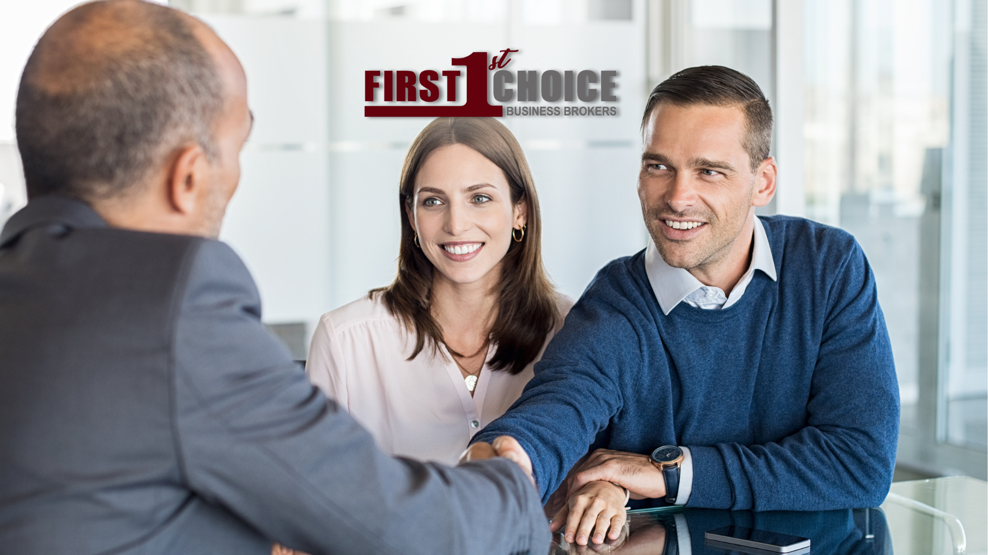 A man and woman are sitting at a table shaking hands with a man in a suit.