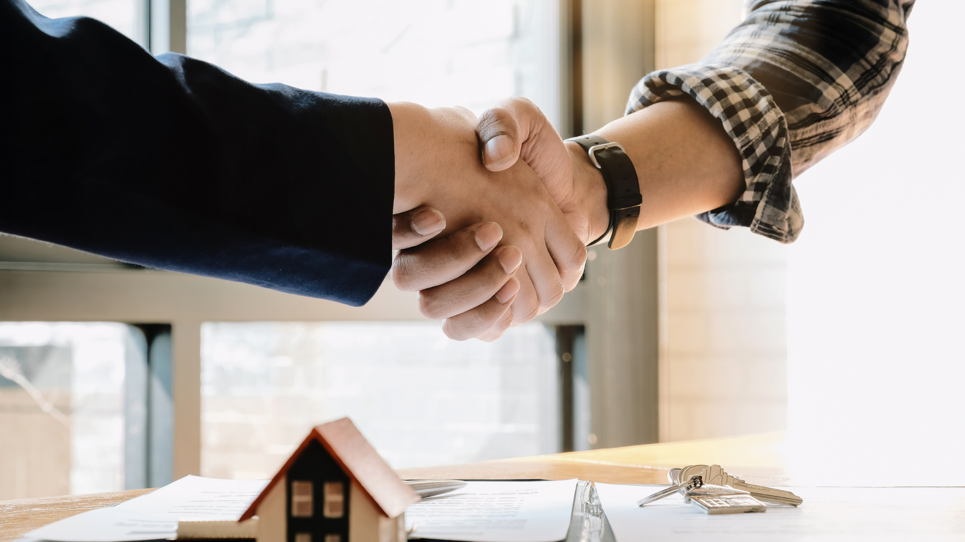 Two people are shaking hands in front of a model house.