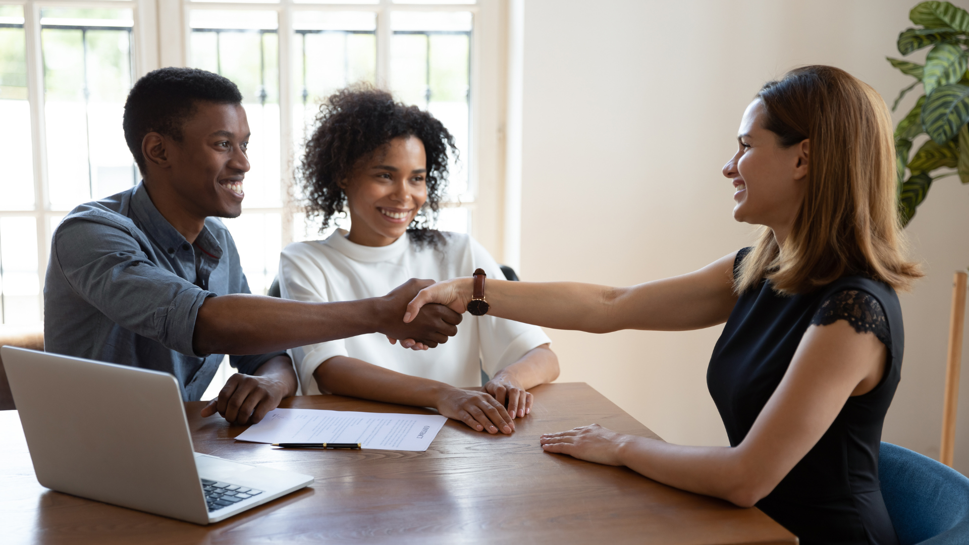 A man and woman are shaking hands with a woman while sitting at a table.