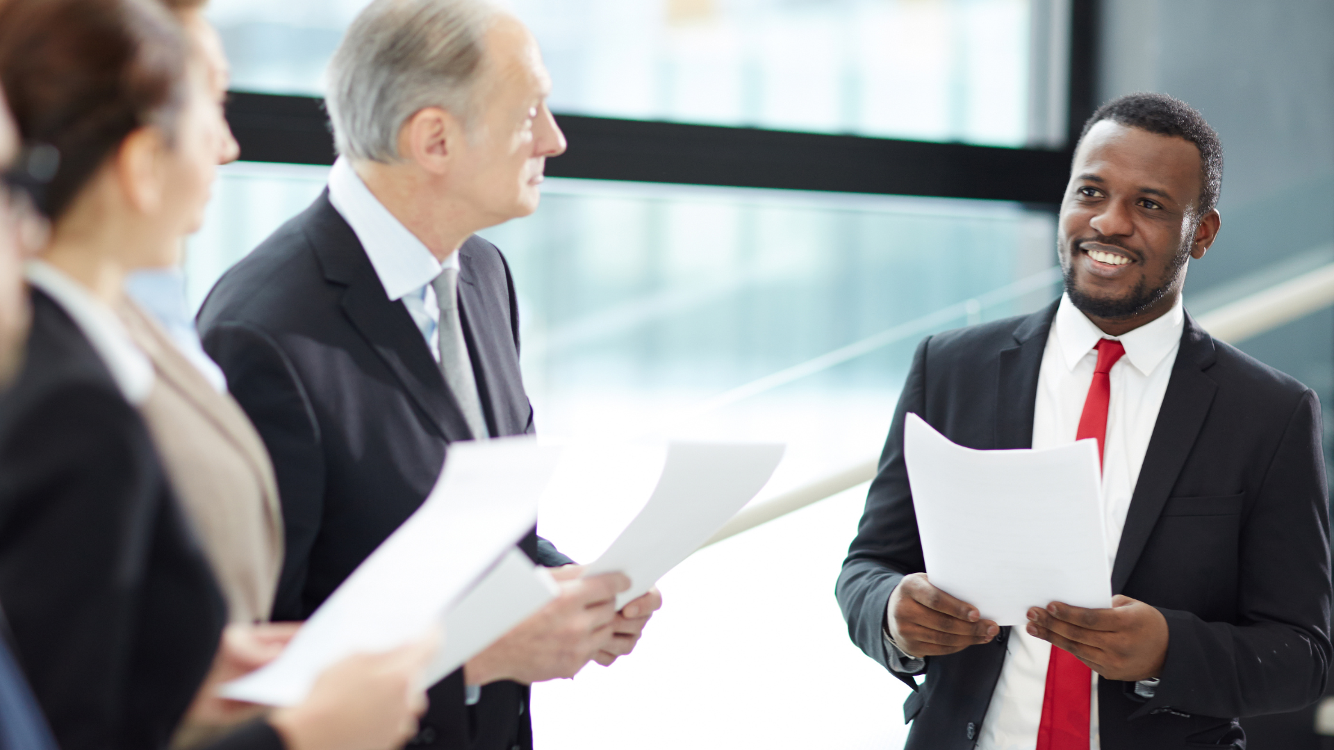 A group of business people are standing around a table holding papers.