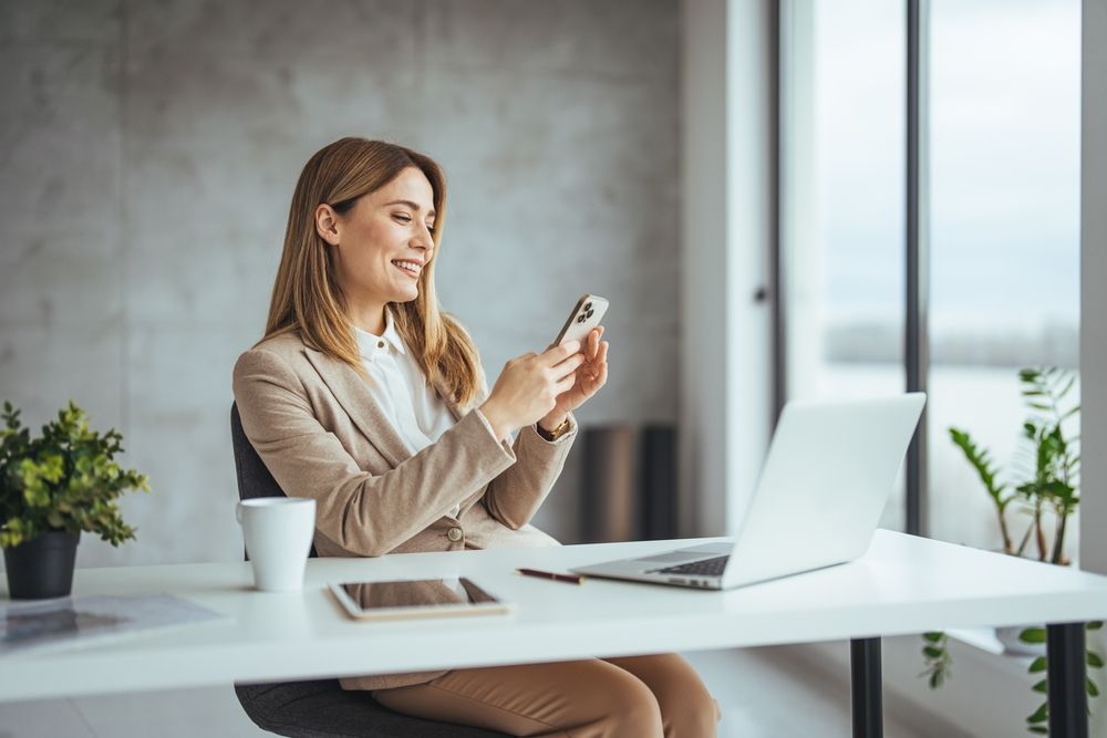 A woman is sitting at a desk looking at her cell phone.