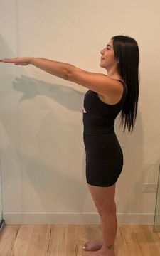 Woman standing, arms outstretched, wearing a black outfit. Standing in front of a wall.