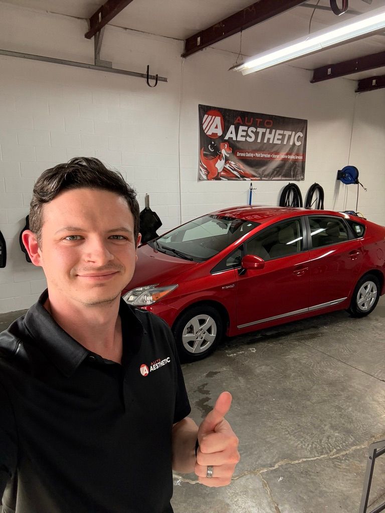 Man giving thumbs up, standing next to red Prius in a garage. Banner reads