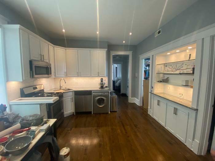 Modern kitchen with white cabinets, stainless steel appliances, and wood floors.