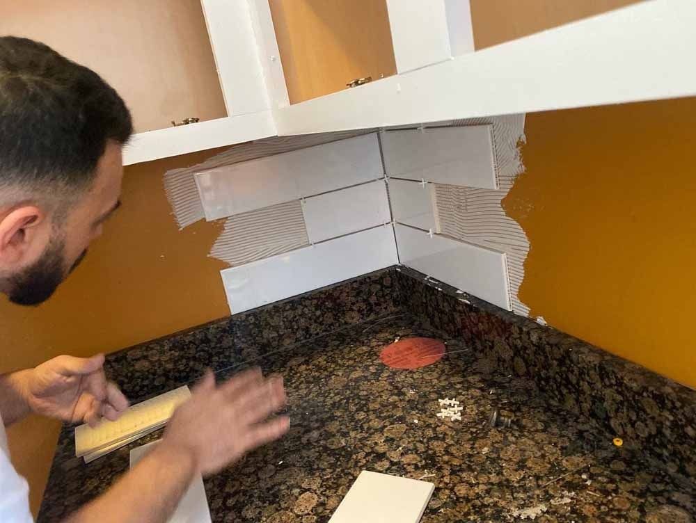 Man tiling a kitchen backsplash, applying tiles to the corner wall.