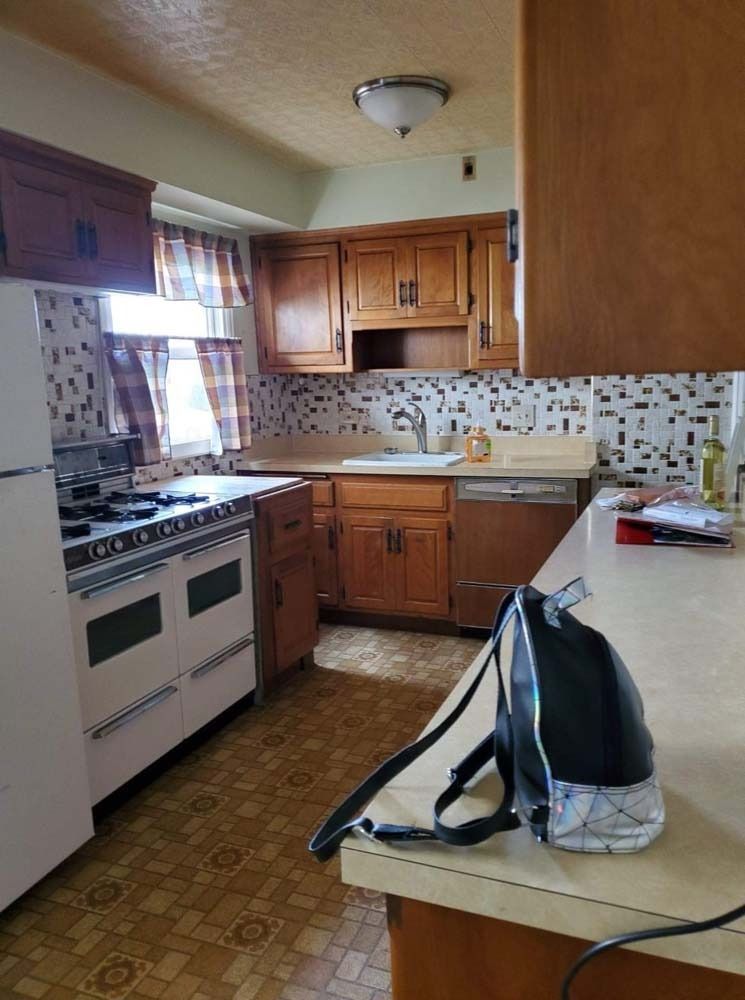 Kitchen with wooden cabinets, a white stove, patterned backsplash, and a backpack on the countertop.