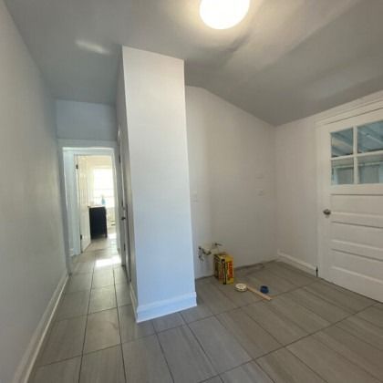 Empty room with tiled floor, white walls, and a door. There is a hallway to another room.