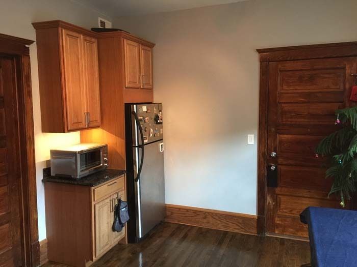 Small kitchen with wooden cabinets, stainless steel refrigerator, microwave, and a wooden door.