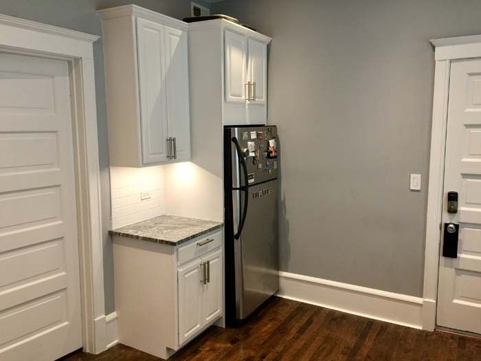 White kitchen cabinets with countertop, refrigerator, and two doors.