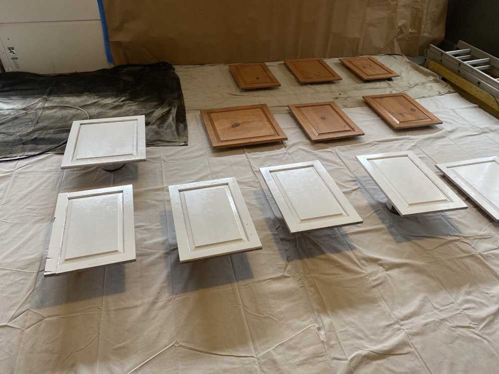Painted kitchen cabinet doors laid out on a drop cloth. Some are white, others a natural wood color.