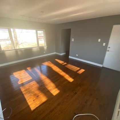 Empty room with dark wood floors, gray walls, sunlight streaming through windows.