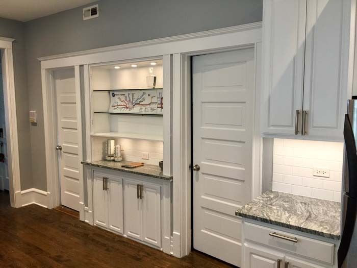 Built-in white kitchen cabinets with glass shelves, a granite countertop, and two doors.