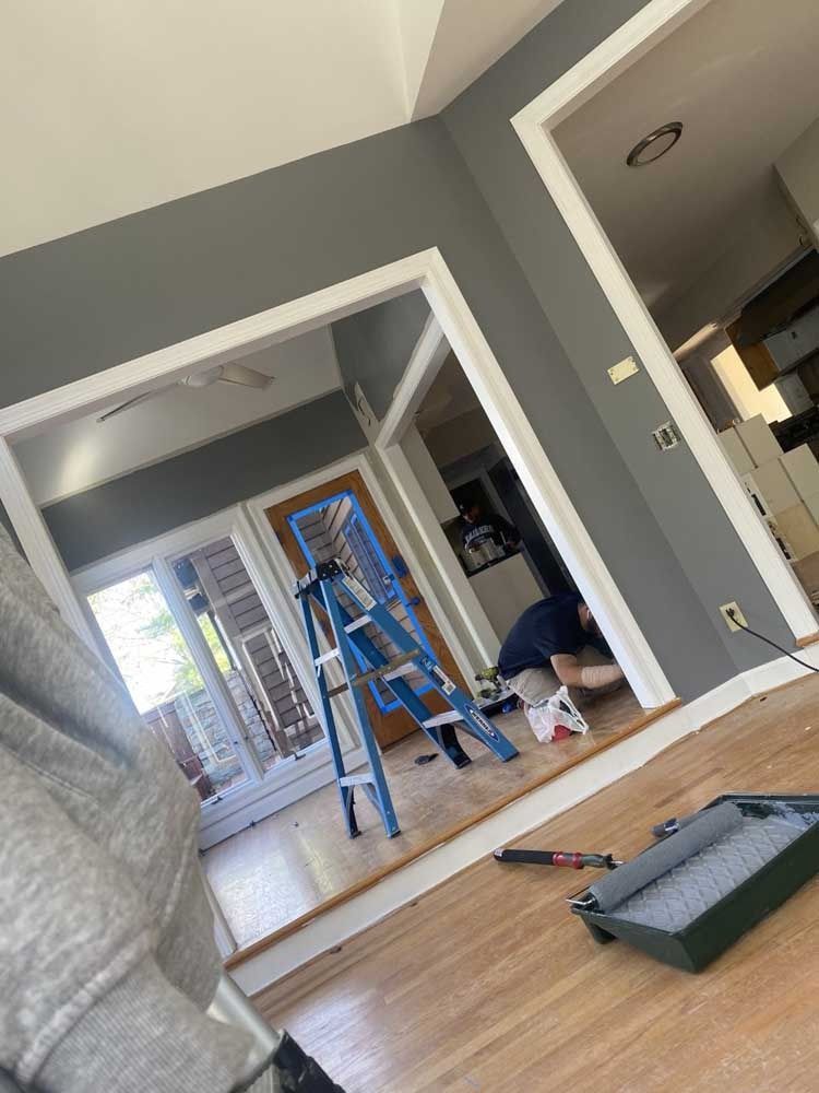 A person painting a room gray with white trim, using a ladder and painting supplies.
