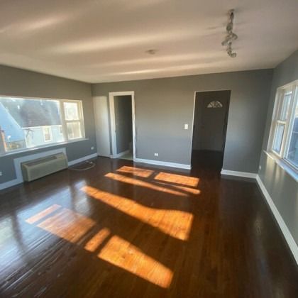 Bright living room with hardwood floors, gray walls, and sunlight streaming through windows.