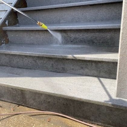 Power washer cleaning gray concrete stairs.