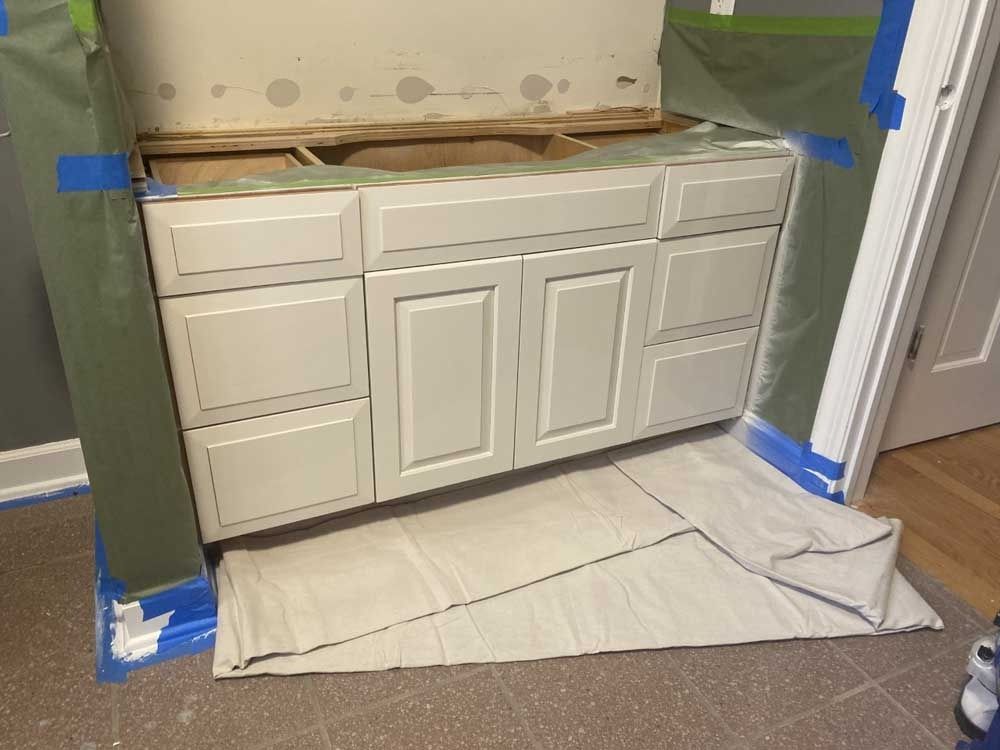 Bathroom cabinet, partially painted gray, with drop cloth and masking, ready for renovation.