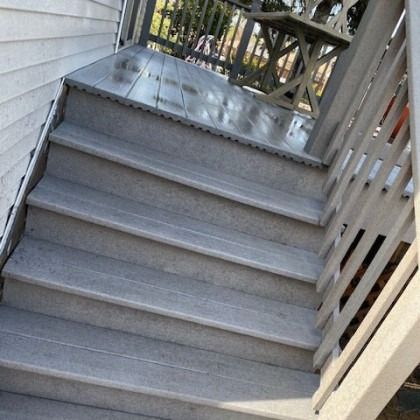 Gray composite stairs leading to a deck with a railing.