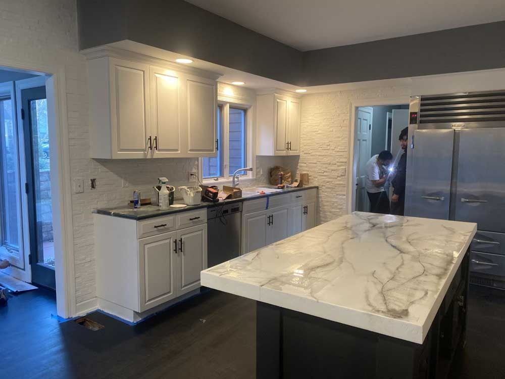 Kitchen remodel with white cabinets, marble island countertop, and tile backsplash.