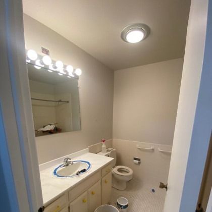 Bathroom with vanity, toilet, and overhead light. White cabinets, beige walls, and a large mirror.