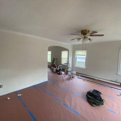 Room being painted, with protective floor covering and painting supplies visible.