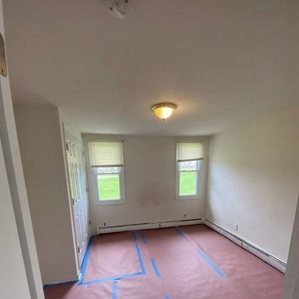 Empty room with two windows, overhead light, and paper-covered floor.