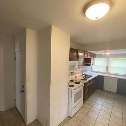 Kitchen with white appliances, dark cabinets, and tile floor. Doorway on the left.