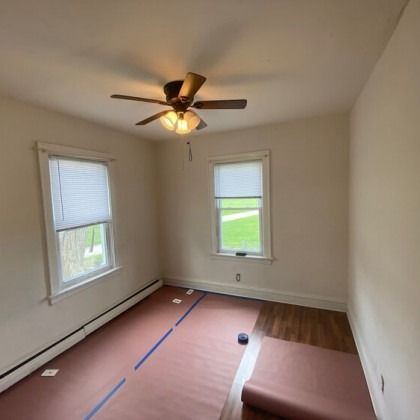 Empty room with windows, ceiling fan, and partially installed flooring; the room is beige.