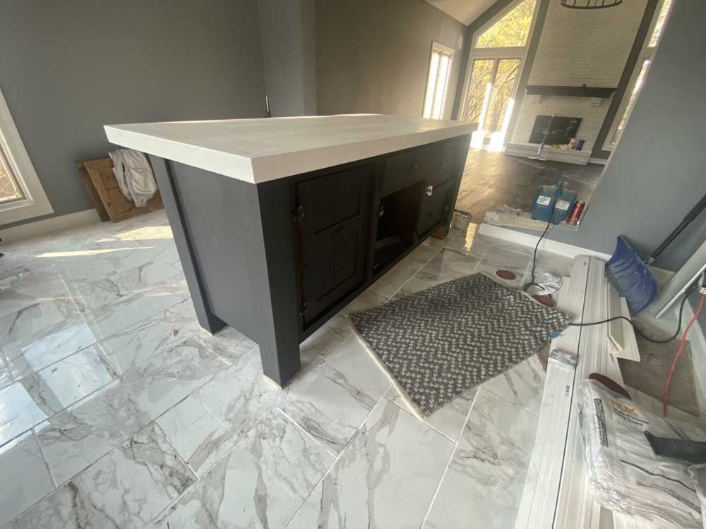 Kitchen island with gray cabinets and white countertop, on tiled floor, with supplies nearby.