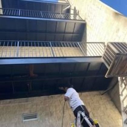 Person on a ladder, working on the underside of a building's balcony.