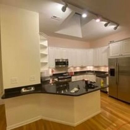 Modern kitchen with white cabinets, black countertop island, and stainless steel refrigerator.