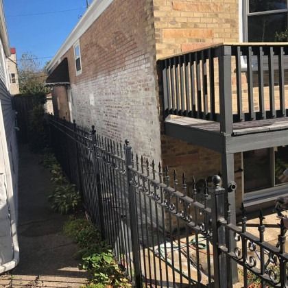 Black metal fence along a narrow alleyway beside a brick building with a deck.