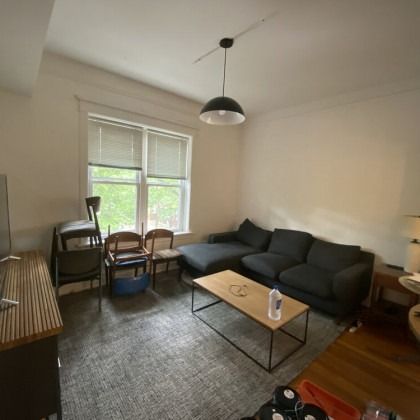 Living room with dark gray sectional, wooden coffee table, rug, window, and chairs.