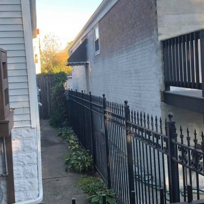 Narrow alleyway between buildings, black metal fence, and a white and brick wall.