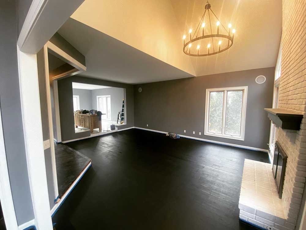 Empty living room with dark gray walls, black floor, and chandelier.