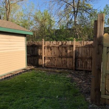 Backyard with weathered wooden fence, shed, and green grass.