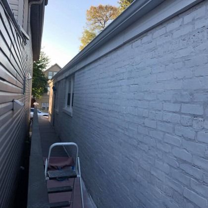 Narrow alley between a painted brick wall and a wood-sided building; a stepladder is in the alley.
