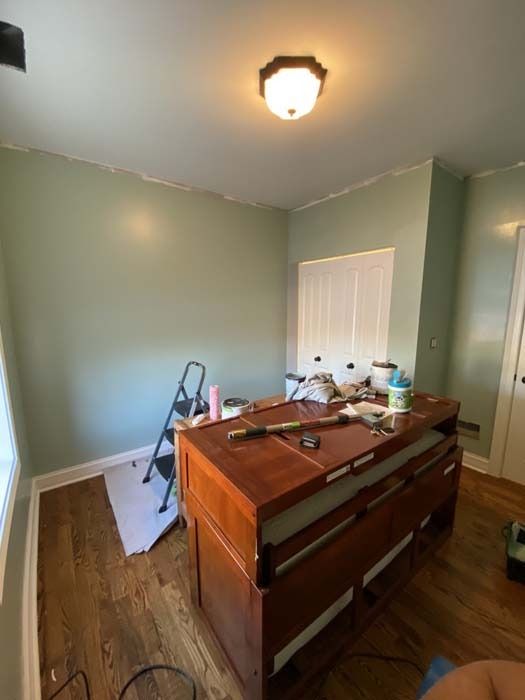 Room with green walls, wood floors, and a wooden island. Tools and supplies are on the island.