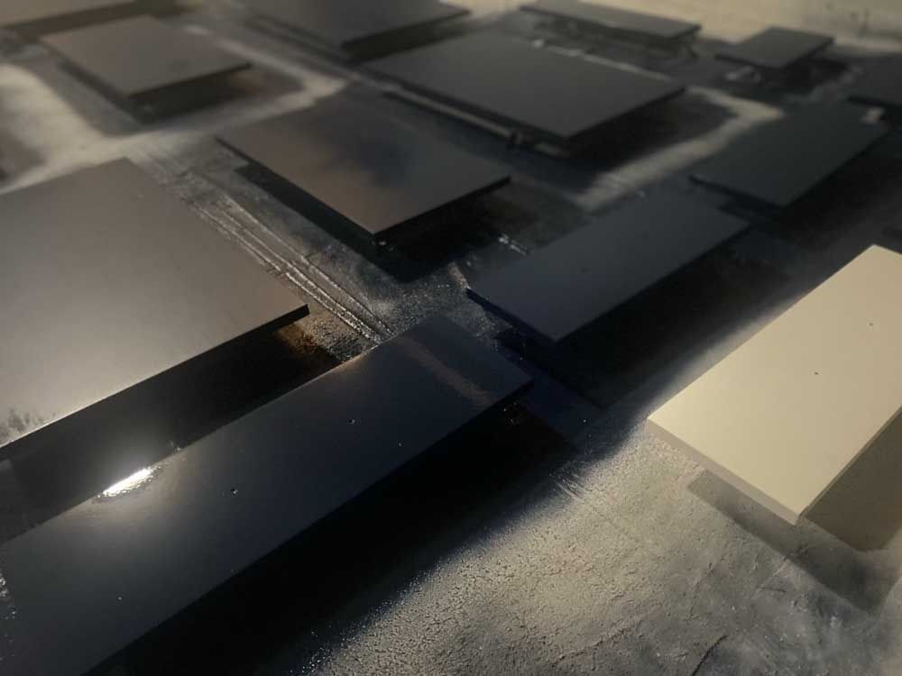 Dark painted wooden rectangles on a surface, drying. One beige rectangle.