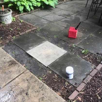 Patio with wet stone tiles, dirt, a red gas can, and a white can.