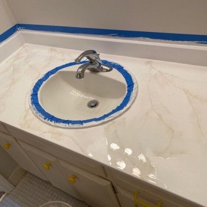 Bathroom vanity with a white sink and marble-like countertop, taped for painting.