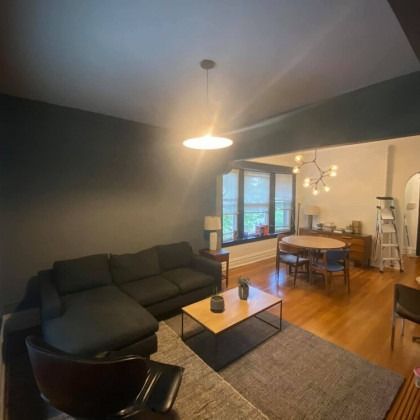 Living room with dark gray sectional, rug, and coffee table. Dining area visible with table and chairs.