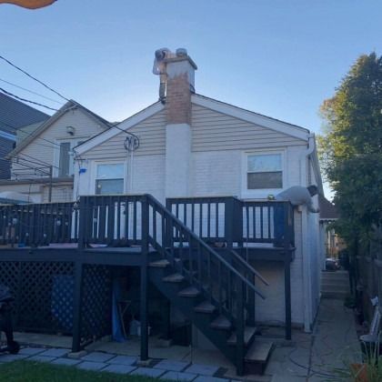 Workers on a chimney and roof of a two-story home with a dark deck and staircase.