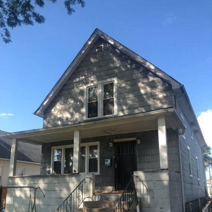 Gray two-story house with a front porch. Overcast sky.